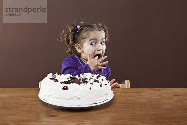 Ein junges Mädchen  das einen Geschmack von einem gefrosteten Kuchen schmuggelt.