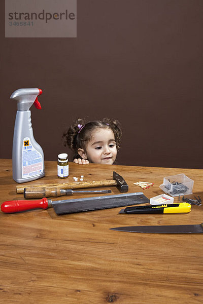 Ein junges Mädchen  das gefährliche Gegenstände auf einem Tisch betrachtet  Studioaufnahme