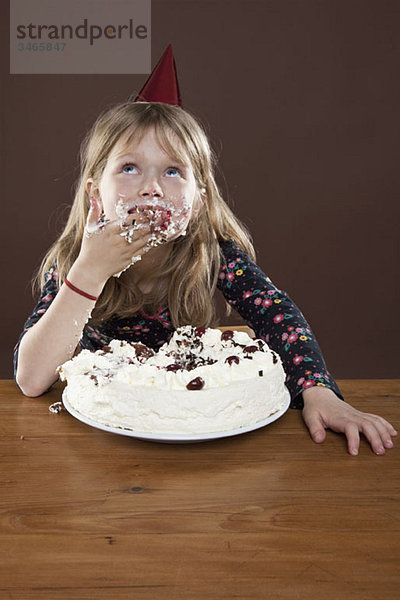 Ein Mädchen mit einem Partyhut  das Kuchen mit den Händen isst  Studioaufnahme