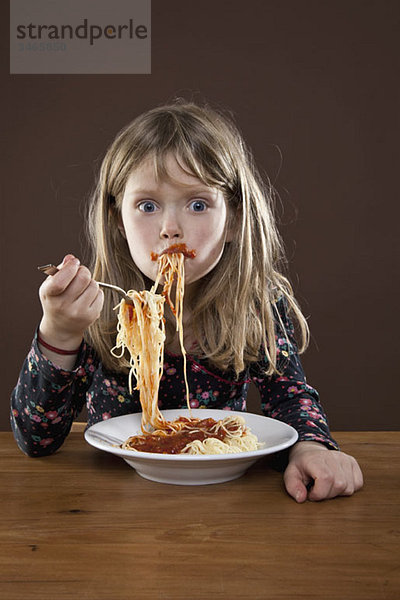 Ein junges Mädchen  das ihr Spaghetti in den Mund schiebt.