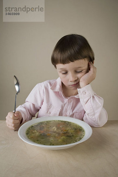 Ein Junge schaut enttäuscht auf eine Schüssel mit Gemüsesuppe.