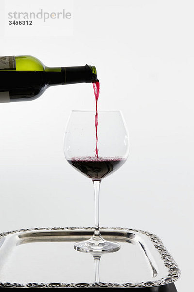 Rotwein  der in ein Weinglas auf einem Tablett gegossen wird.