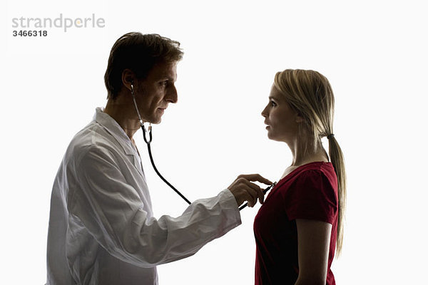 Ein Arzt  der mit einem Stethoskop eine Untersuchung an einem Patienten durchführt.