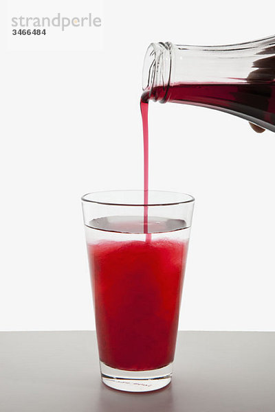 Detail eines Fruchtsirups  der in ein Glas Wasser gegossen wird.