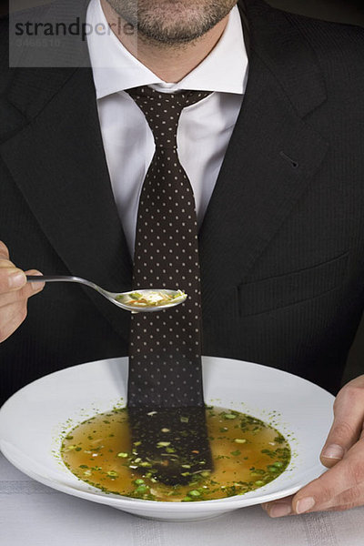 Mann am Tisch sitzend mit Krawatte in einer Schüssel Suppe schwimmend