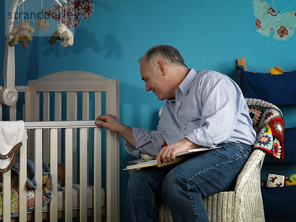 Erwachsener Mann sitzend mit Baby im Kinderbett