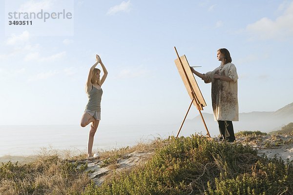 Junger Mann malt Mädchen in Landschaft
