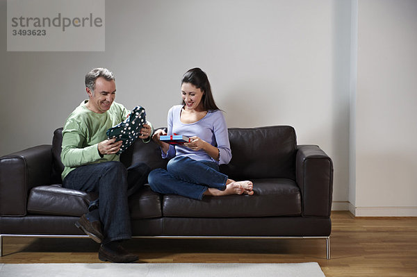 Lächelndes Paar tauscht Geschenke auf der Couch aus