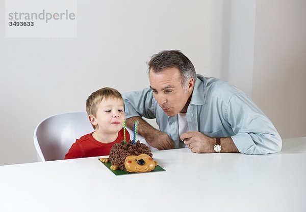 Junge mit Vater  der Kerzen auf Kuchen ausbläst.