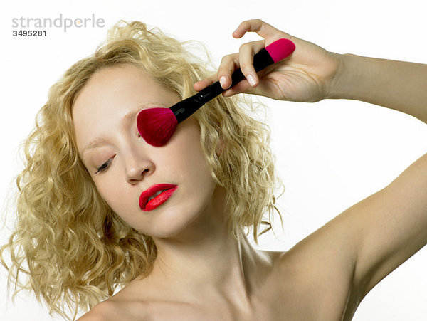 Junge Frau beim Auftragen von Lidschatten mit Make-up-Pinsel