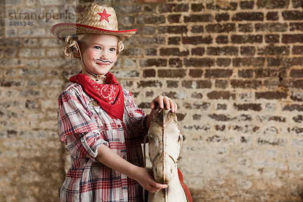 Junges Mädchen verkleidet als Cowgirl mit Schaukelpferd