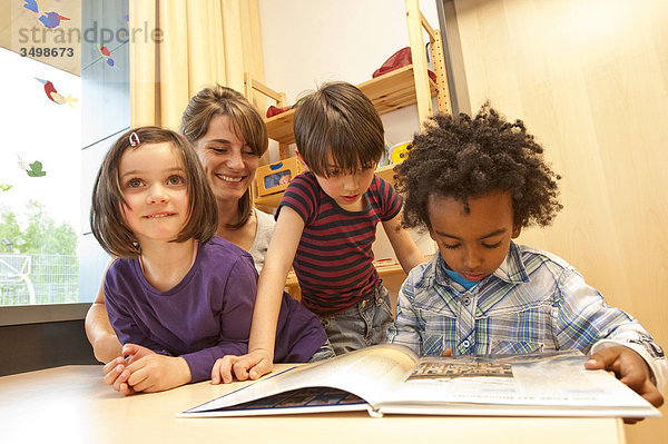Kindergärtnerin und Kinder schauen sich ein Buch an  Flachwinkelansicht