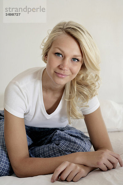 Portrait einer jungen Frau in Pyjamas sitzen auf dem Bett