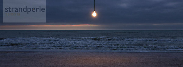 Glühbirne über dem Strand bei Sonnenuntergang beleuchtet