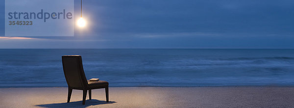 Glühbirne über Stuhl am Strand bei Nacht beleuchtet