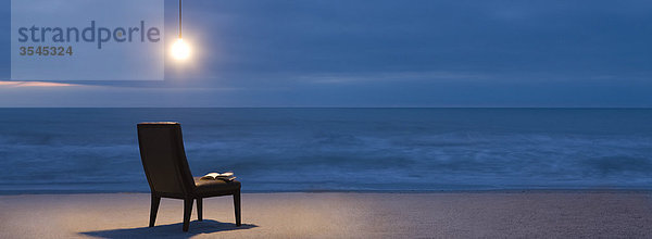 Glühbirne über Stuhl am Strand bei Nacht beleuchtet