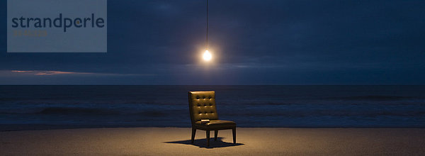 Glühbirne über Stuhl am Strand bei Nacht beleuchtet