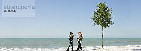 Kinder stehen mit Gartengeräten neben einem Baum  der am Strand gepflanzt wurde.