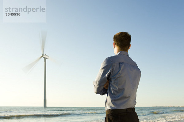Mann am Strand beobachtet Offshore-Windkraftanlage bei der Arbeit