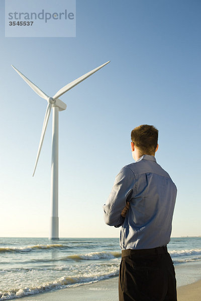 Geschäftsmann am Strand mit Blick auf Offshore-Windkraftanlage