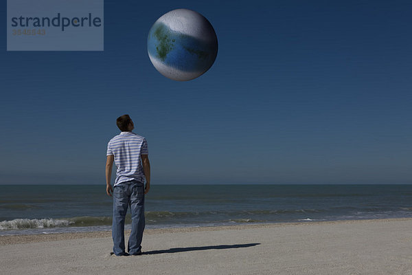 Mann am Strand blickt auf die außerirdische Welt  die sich im Orbit befindet