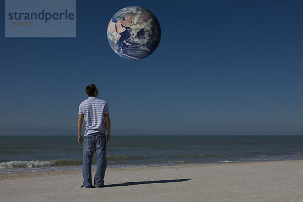 Mann am Strand blickt auf den Planeten Erde und umkreist die Erde
