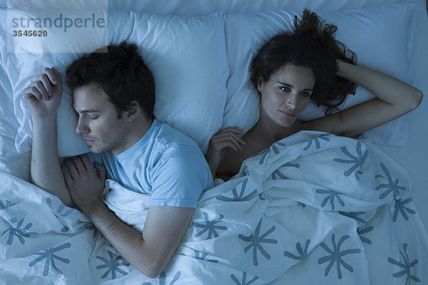 Paar liegt zusammen im Bett  Frau unruhig wach und schaut weg.