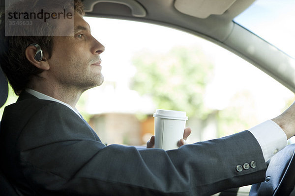 Geschäftsmann  der mit einer Tasse Kaffee in der Hand zur Arbeit fährt.