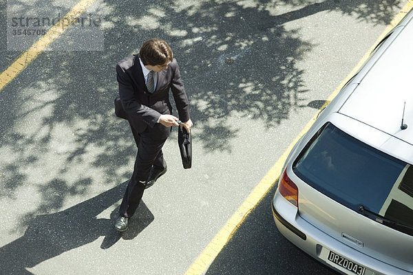 Mann verriegelt Autotüren mit Schlüsselfernbedienung  während er weggeht