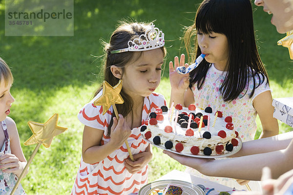 Mädchen bläst Kerzen auf Geburtstagskuchen bei einer Geburtstagsparty im Freien aus.
