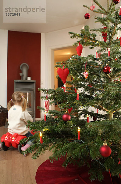 Weihnachtsbaum und Mädchen auf Bobbycar im Wohnzimmer