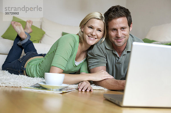 Paar liegt auf dem Fußboden und schaut auf Laptop