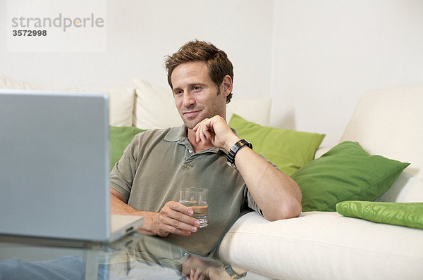 Zufriedener Mann im Wohnzimmer schaut auf Laptop