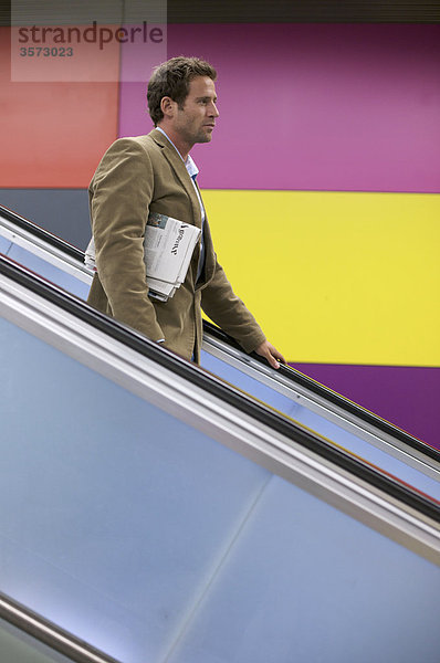 Mann mit Zeitung auf einer Rolltreppe