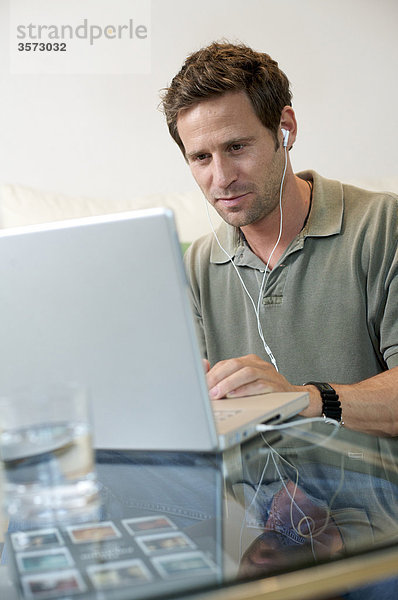 Mann mit Ohrstöpseln benutzt Laptop