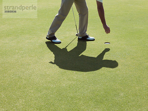 Mann spielt Golf  nimmt den Ball auf.