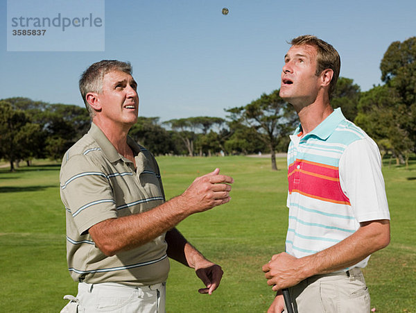 Zwei reife Männer spielen zusammen Golf und werfen eine Münze.