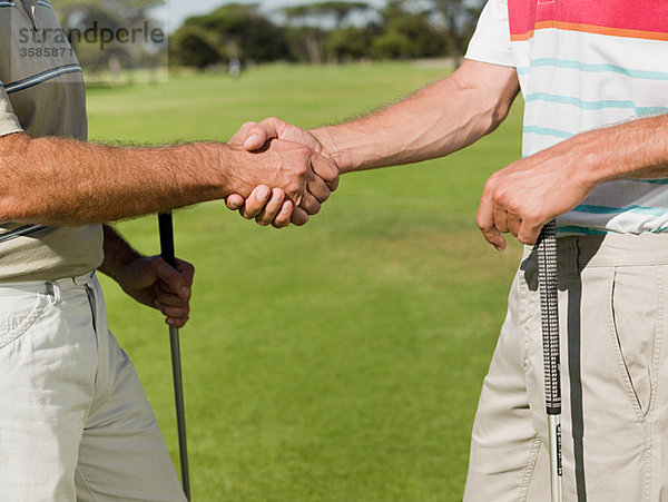 Zwei reife Männer beim Händeschütteln auf dem Golfplatz