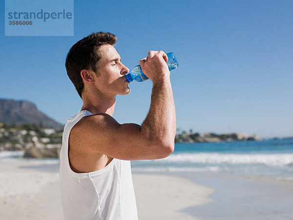 Junger Mann trinkt Wasser am Strand