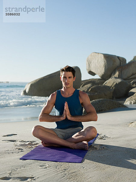 Junger Mann beim Yoga am Strand