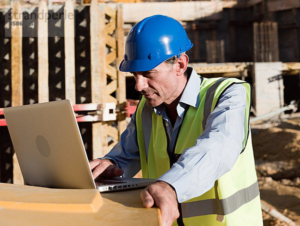 Erwachsener Mann mit Laptop auf der Baustelle