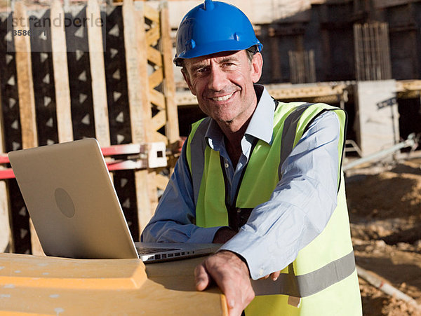 Erwachsener Mann mit Laptop auf der Baustelle