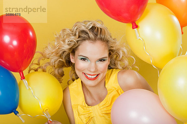 Junge blonde Frau mit Luftballons vor gelbem Hintergrund