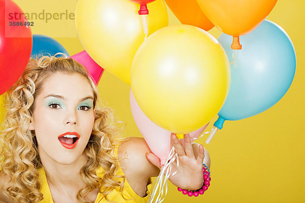 Junge blonde Frau mit Luftballons vor gelbem Hintergrund
