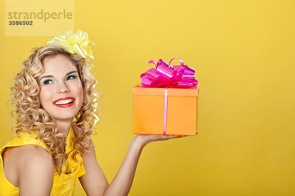 Junge blonde Frau mit Geburtstagsgeschenk vor gelbem Hintergrund