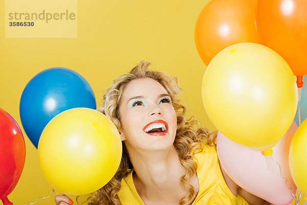 Junge blonde Frau mit Luftballons vor gelbem Hintergrund