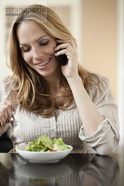 Frau auf dem Handy isst Salat