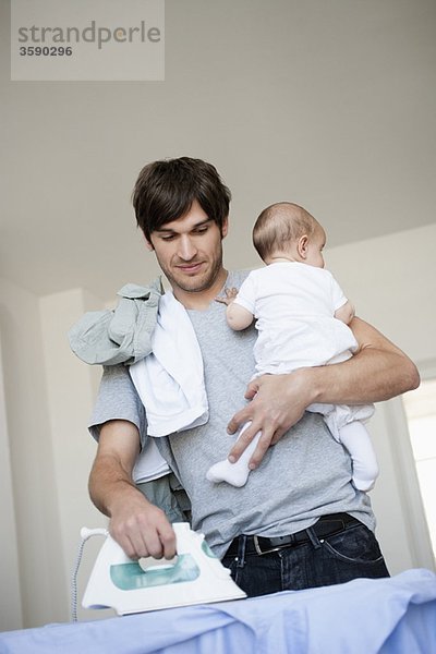 Vater mit Baby im Arm bügeln