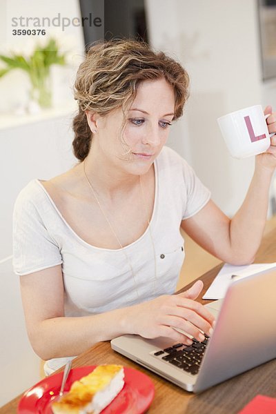 Frau auf ihrem Laptop mit einer Tasse Kaffee