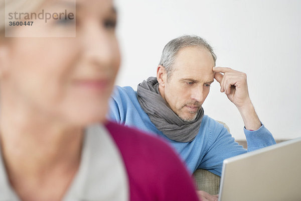 Nahaufnahme einer Frau mit einem Mann  der im Hintergrund an einem Laptop arbeitet.